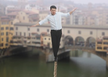 Concentrated businessman walking rope over city. Concept of risk and balance