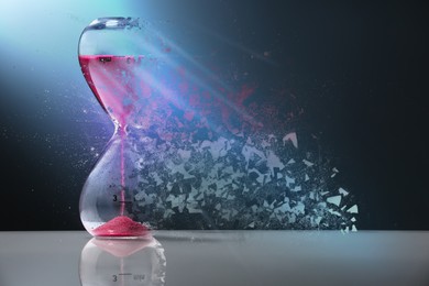 Image of Hourglass dissolving on table against dark background. Fleeting time