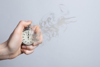 Image of Woman holding dissolving chronometer on grey background, closeup. Time is running out