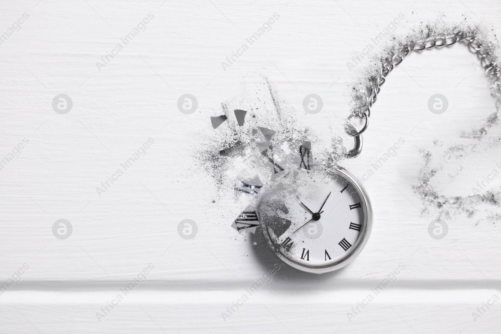 Image of Vintage pocket watch with chain dissolving on white wooden background, top view. Fleeting time
