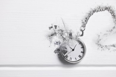 Vintage pocket watch with chain dissolving on white wooden background, top view. Fleeting time