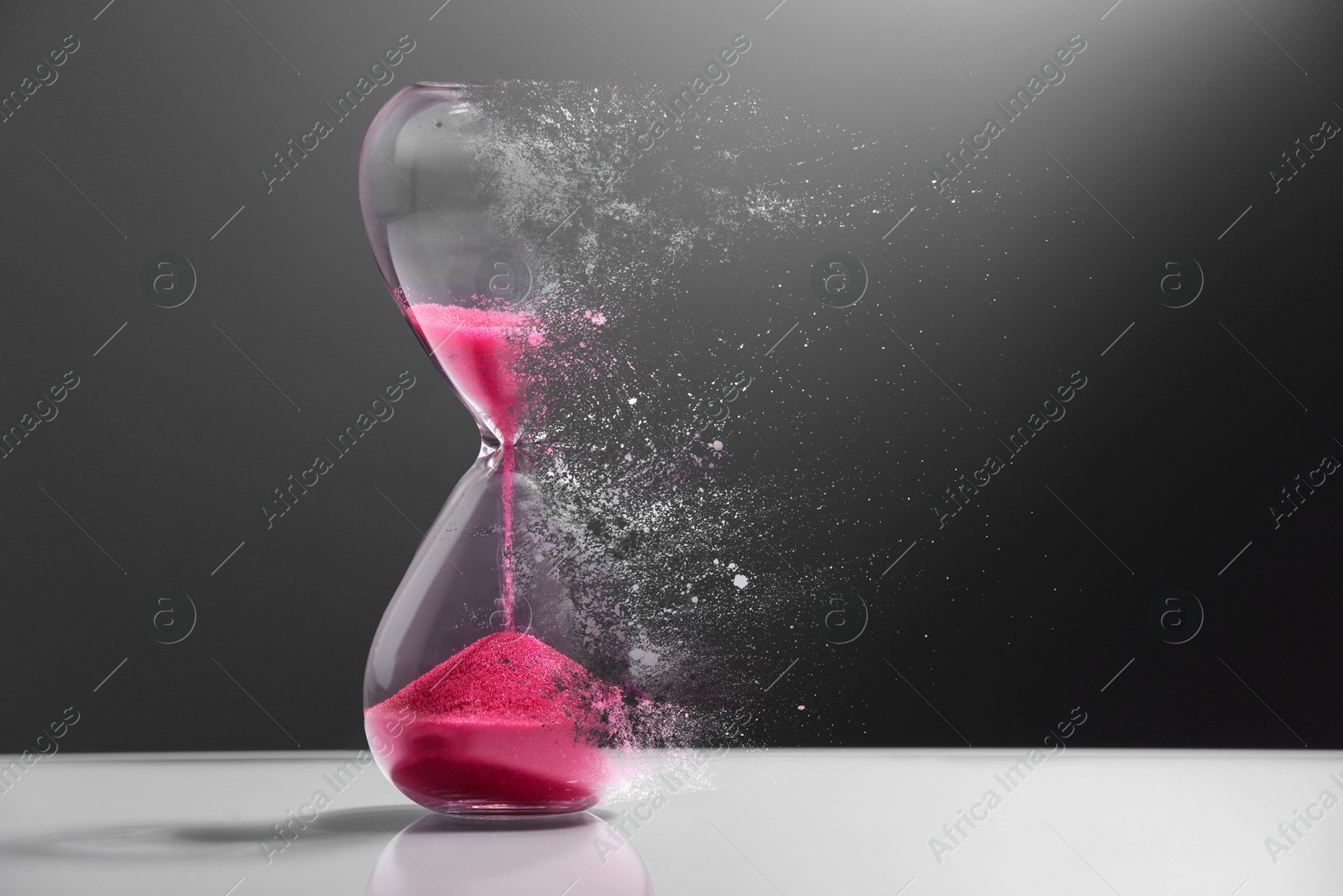 Image of Hourglass dissolving on table against dark background. Fleeting time