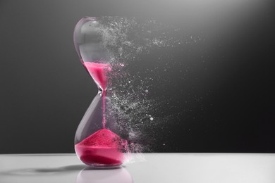 Image of Hourglass dissolving on table against dark background. Fleeting time