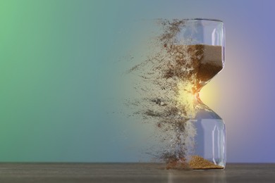 Image of Hourglass dissolving on table against color background. Fleeting time