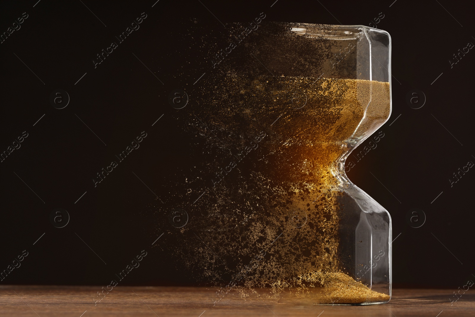 Image of Hourglass dissolving on table against black background. Fleeting time