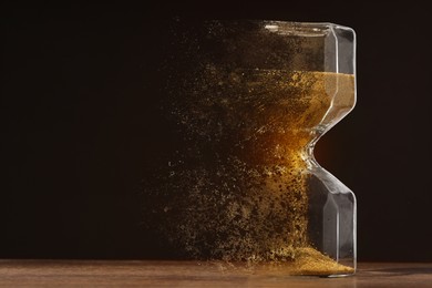 Hourglass dissolving on table against black background. Fleeting time