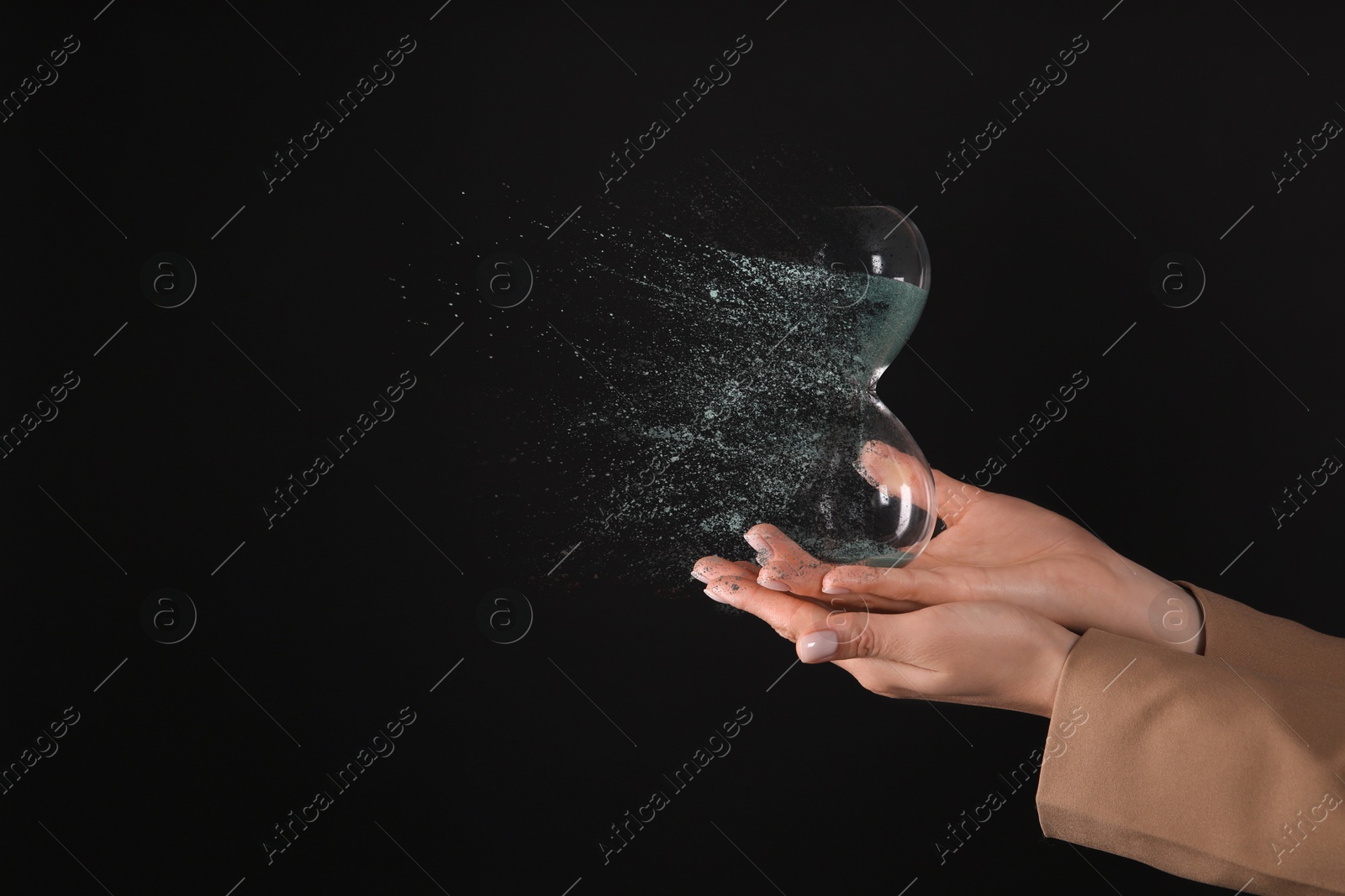 Image of Businesswoman holding dissolving hourglass on black background, closeup. Time is running out