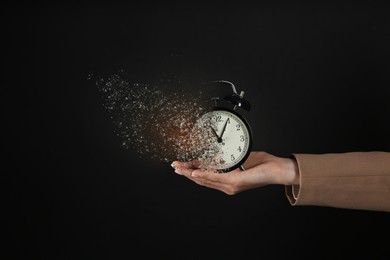 Businesswoman holding dissolving alarm clock on black background, closeup. Time is running out