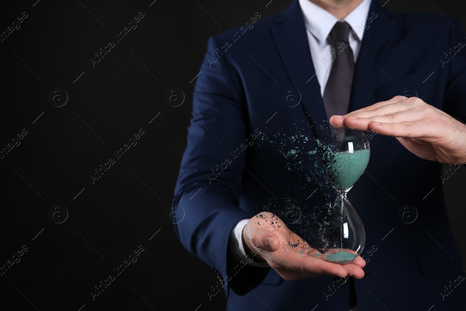 Image of Businessman holding dissolving hourglass on black background, closeup. Time is running out