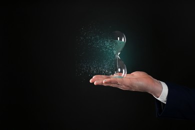 Businessman holding dissolving hourglass on black background, closeup. Time is running out