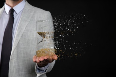 Image of Businessman holding dissolving hourglass on black background, closeup. Time is running out