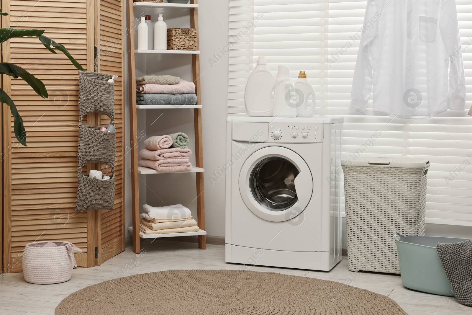 Photo of Washing machine, detergents, towels, baskets and folding screen in laundry room