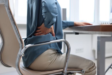 Photo of Woman suffering from back pain in office, closeup. Symptom of poor posture