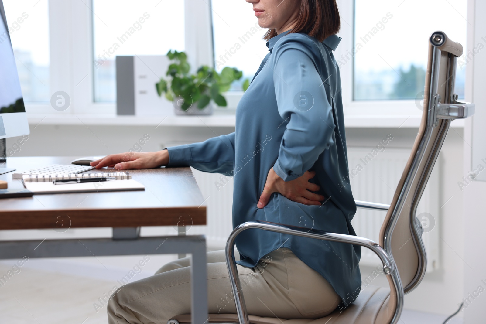 Photo of Woman suffering from back pain in office, closeup. Symptom of poor posture