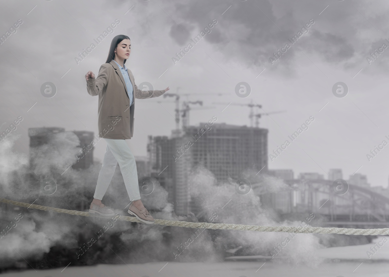 Image of Concentrated businesswoman walking rope over city. Concept of risk and balance