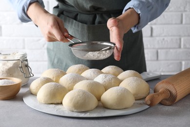 Woman sprinkling flour over dough balls at grey table, closeup