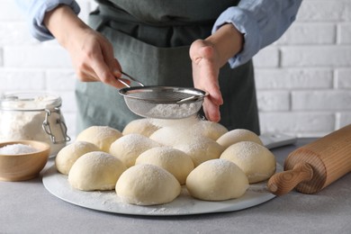 Woman sprinkling flour over dough balls at grey table, closeup