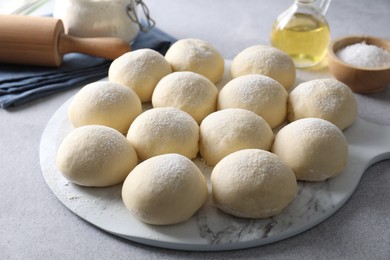 Photo of Raw dough balls, rolling pin, oil and salt on light grey table