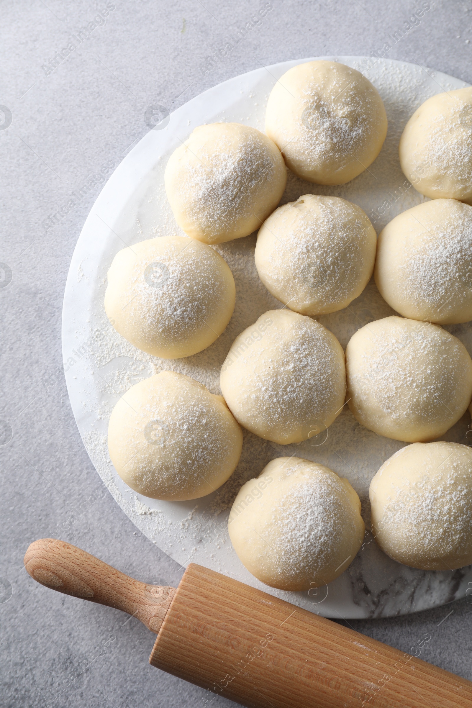 Photo of Raw dough balls and rolling pin on light grey table, top view