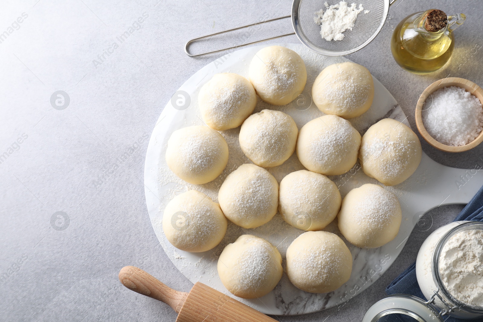 Photo of Raw dough balls, ingredients and rolling pin on light grey table, top view. Space for text