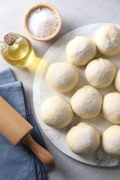 Raw dough balls, ingredients and rolling pin on light grey table, top view