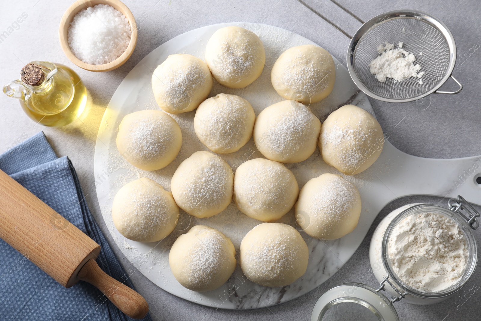 Photo of Raw dough balls, ingredients and rolling pin on light grey table, top view