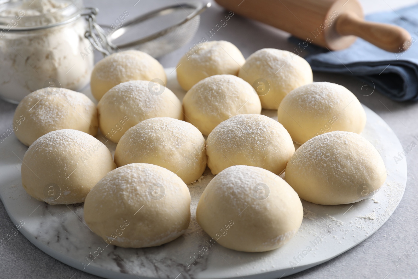 Photo of Raw dough balls, flour and rolling pin on light grey table