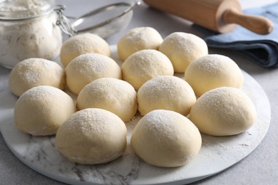 Photo of Raw dough balls, flour and rolling pin on light grey table