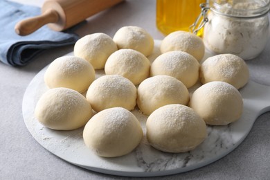 Photo of Raw dough balls, flour and rolling pin on light grey table