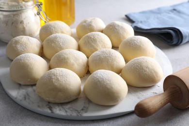 Photo of Raw dough balls, flour and rolling pin on light grey table