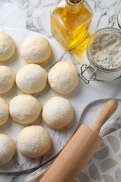 Photo of Raw dough balls, flour, rolling pin and oil on white marble table, top view