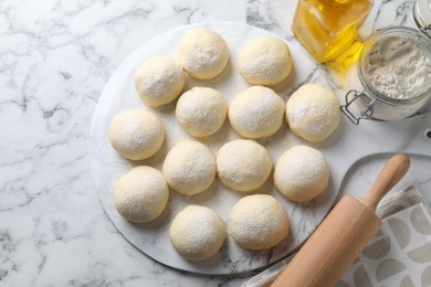 Raw dough balls, flour, rolling pin and oil on white marble table, top view