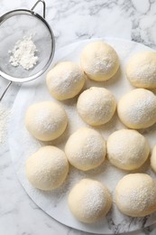 Photo of Raw dough balls, flour and sieve on white marble table, top view