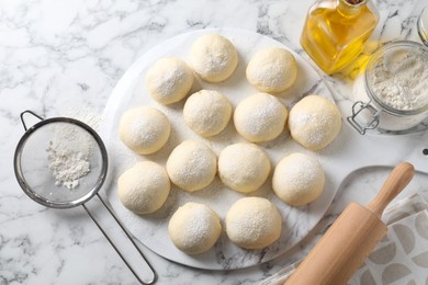 Photo of Raw dough balls, flour, rolling pin and oil on white marble table, top view