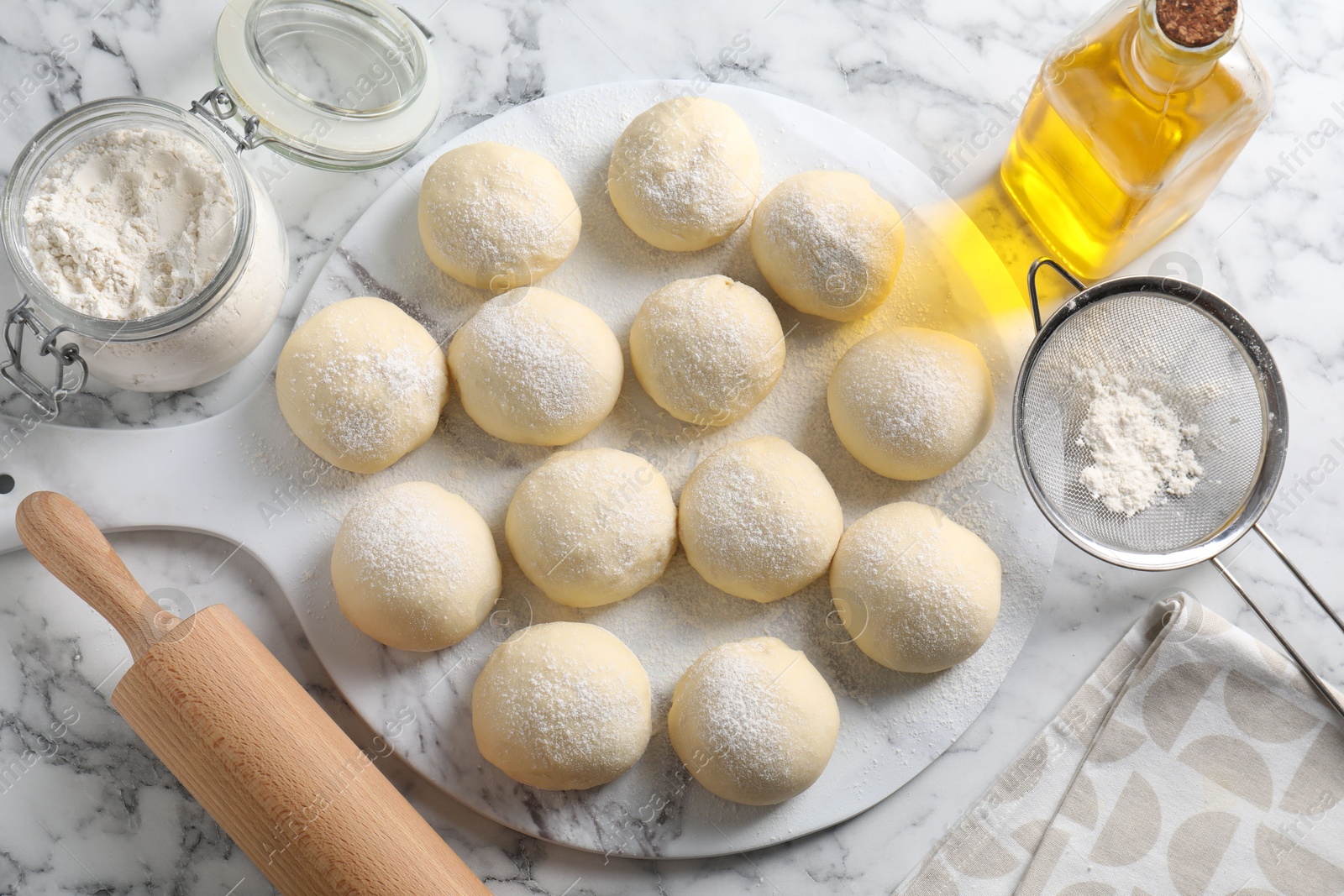 Photo of Raw dough balls, flour, rolling pin and oil on white marble table, top view