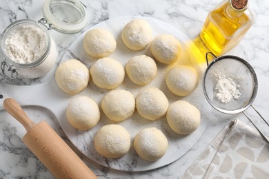 Photo of Raw dough balls, flour, rolling pin and oil on white marble table, top view