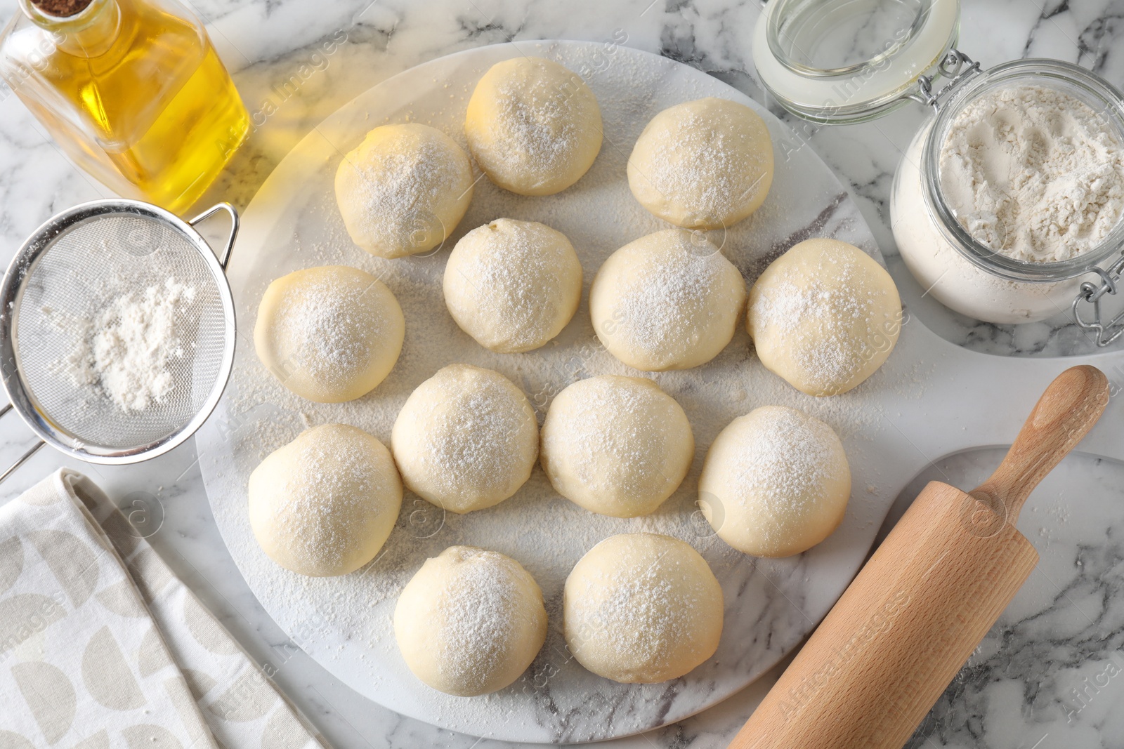 Photo of Raw dough balls, flour, rolling pin and oil on white marble table, top view