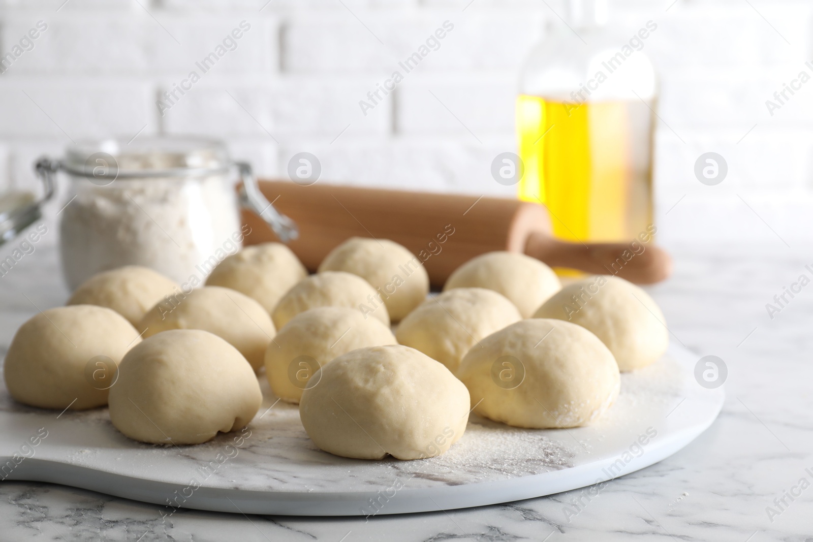 Photo of Raw dough balls, flour, rolling pin and oil on white marble table