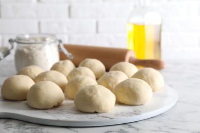 Raw dough balls, flour, rolling pin and oil on white marble table