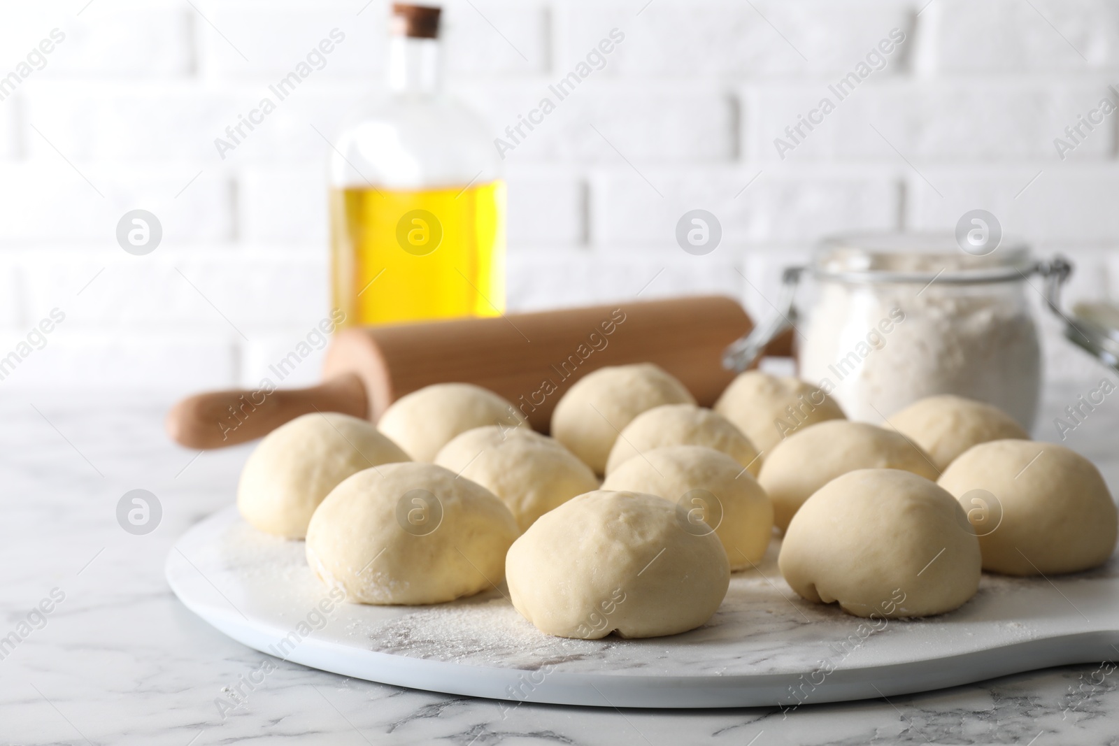 Photo of Raw dough balls, flour, rolling pin and oil on white marble table