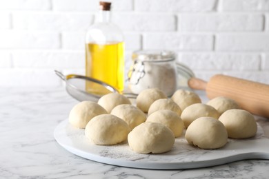 Photo of Raw dough balls, flour, rolling pin and oil on white marble table