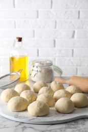 Photo of Raw dough balls, flour, rolling pin and oil on white marble table