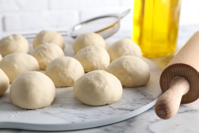 Photo of Raw dough balls and rolling pin on white marble table