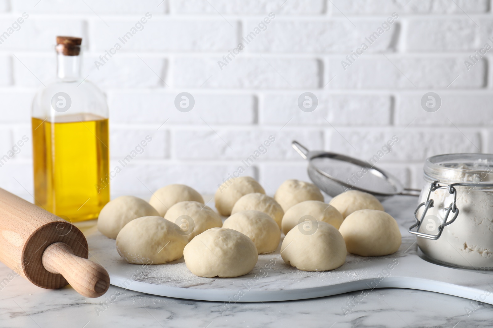 Photo of Raw dough balls, flour, rolling pin and oil on white marble table