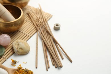 Photo of Incense sticks, Tibetan singing bowl, stones and dry flowers on white table, space for text