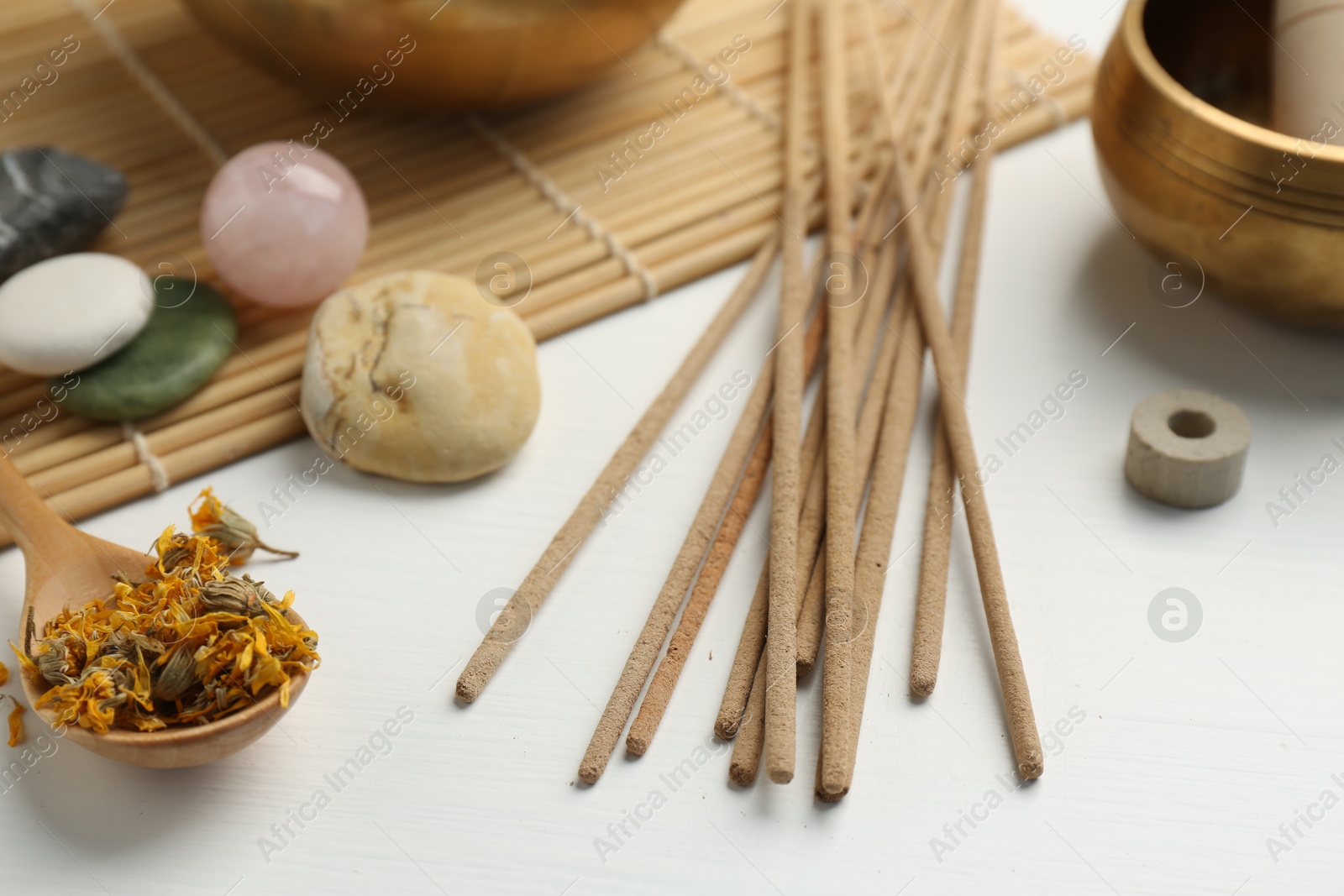 Photo of Incense sticks, stones, dry flowers and Tibetan singing bowl on white table