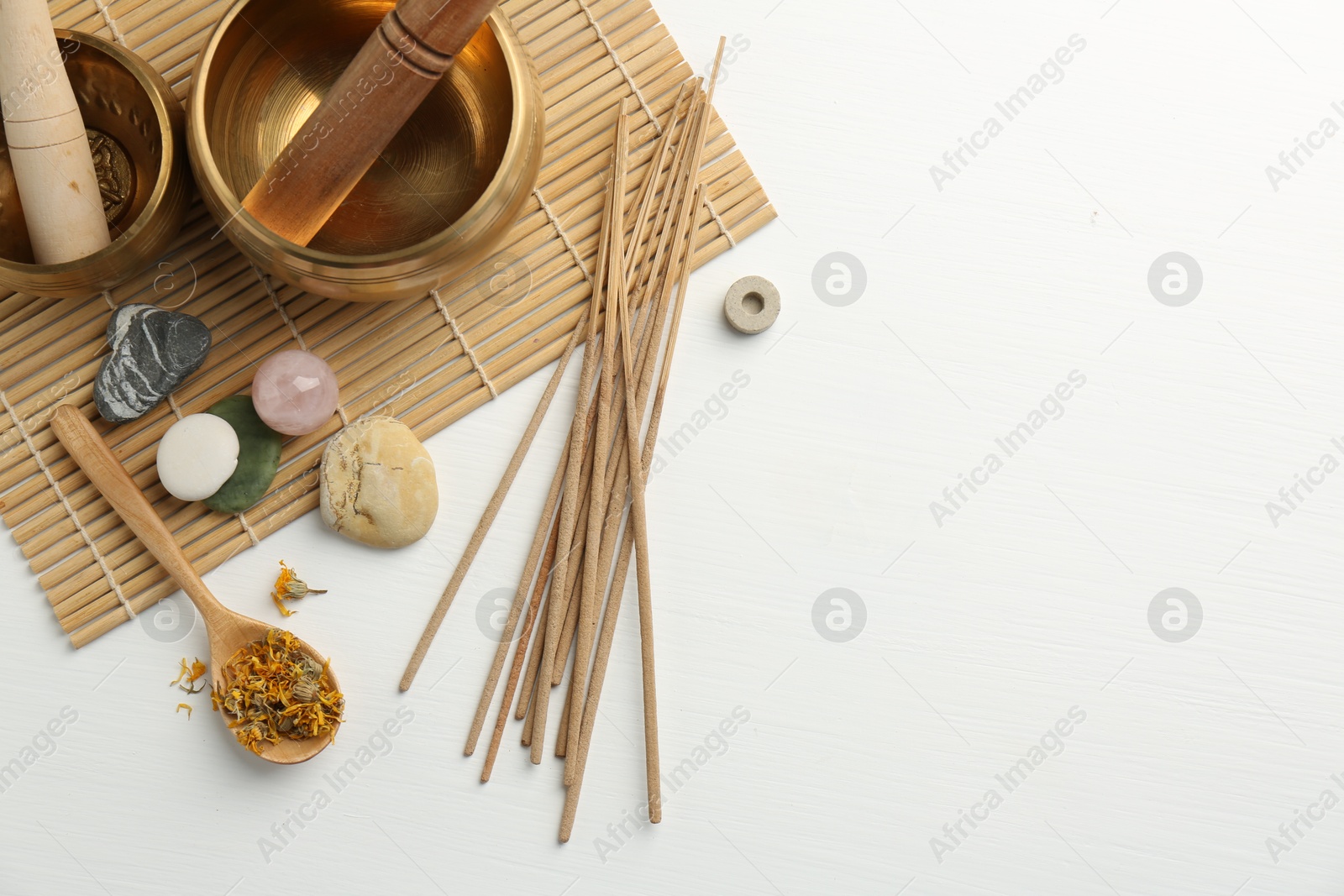 Photo of Incense sticks, Tibetan singing bowls, dry flowers and stones on white wooden table, top view. Space for text