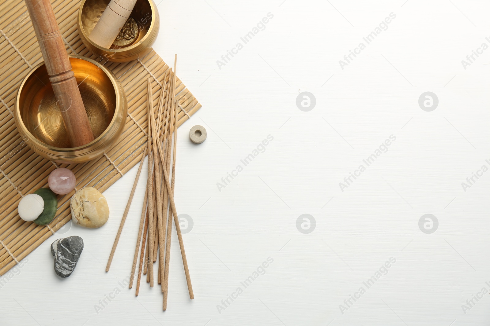 Photo of Incense sticks, Tibetan singing bowls and stones on white wooden table, top view. Space for text