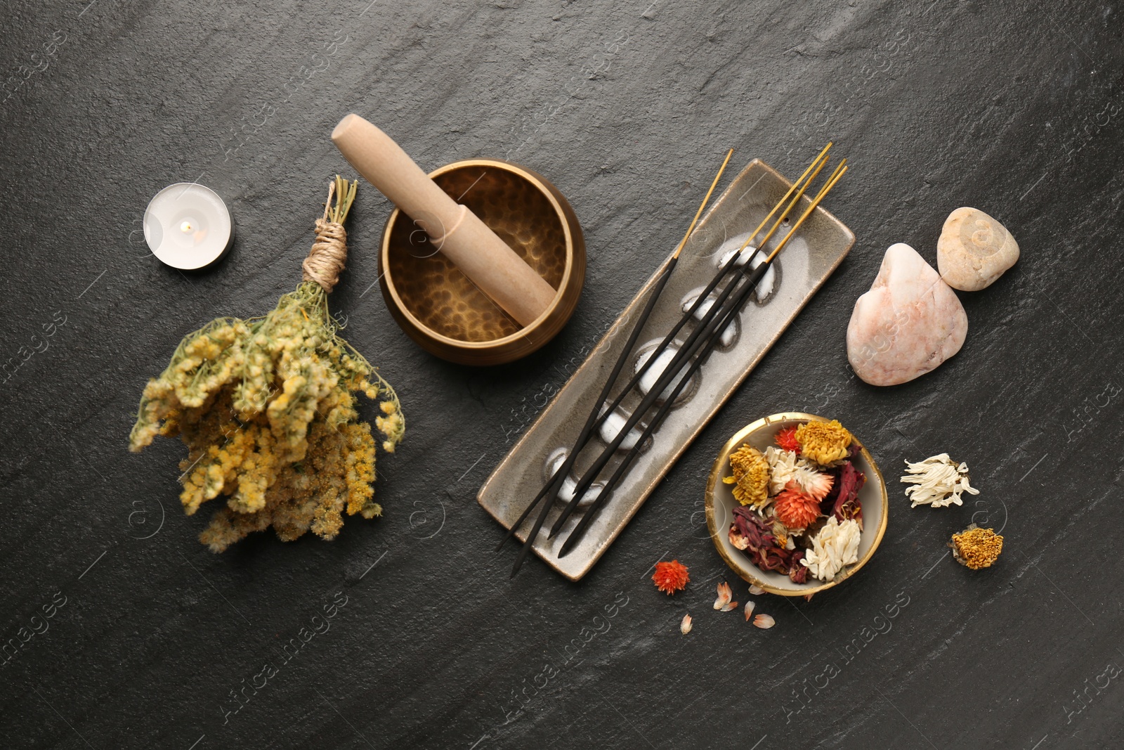 Photo of Incense sticks, Tibetan singing bowl, stones, dry flowers and candle on black table, flat lay