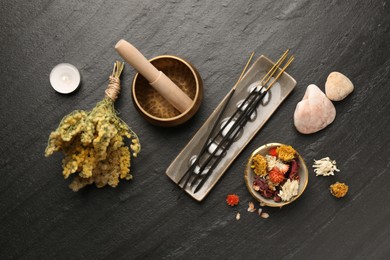 Incense sticks, Tibetan singing bowl, stones, dry flowers and candle on black table, flat lay